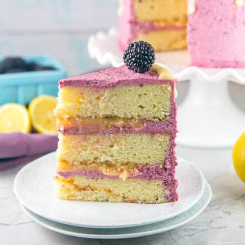 Lemon Curd Cake with Blackberry Buttercream Frosting: a triple level layer cake with lemon cake from scratch, filled with homemade lemon curd, and covered in fresh blackberry frosting and a lemon glaze. The perfect homemade birthday cake for lemon lovers! #bunsenburnerbakery #lemoncake #lemoncurd #layercake #birthdaycake