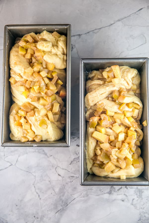 overhead photo of two loaf pans with honey apple babka dough twisted and filled with apples before baking