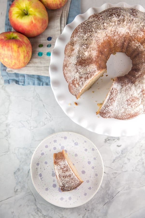 an apple cider donut flavored bundt cake with one slice removed and served on a purple polka dot dessert plate