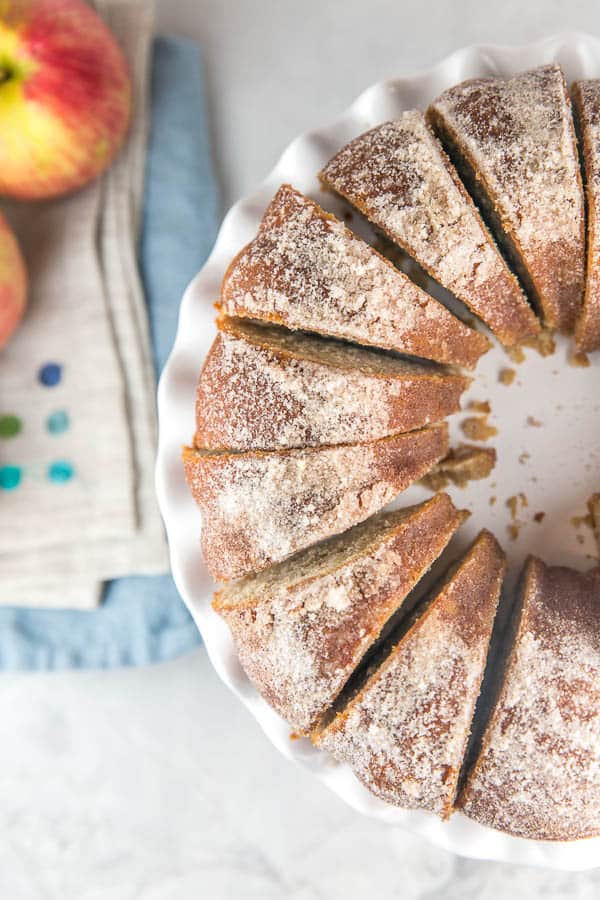 apple cider donut cake cut into slices on a white fluted cake plate