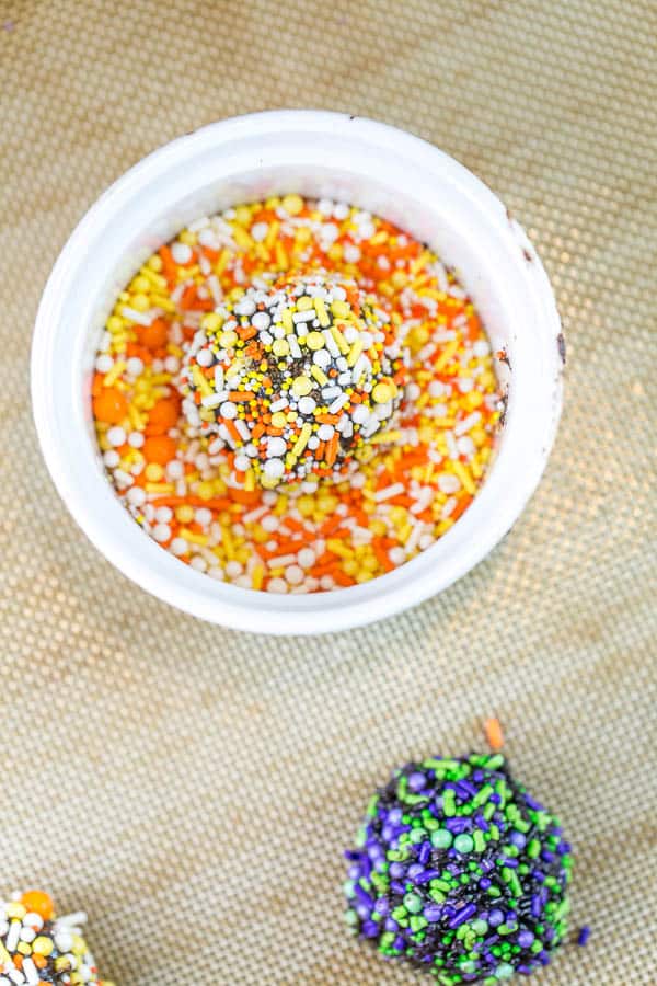 a ball of chocolate cookie dough in the middle of a white bowl filled with orange, white, and yellow sprinkles.