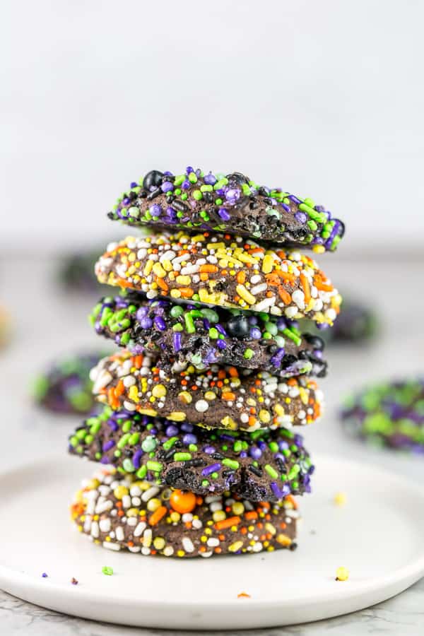 a stack of chocolate fudge cookies covered in halloween sprinkles stacked vertically on a white plate.