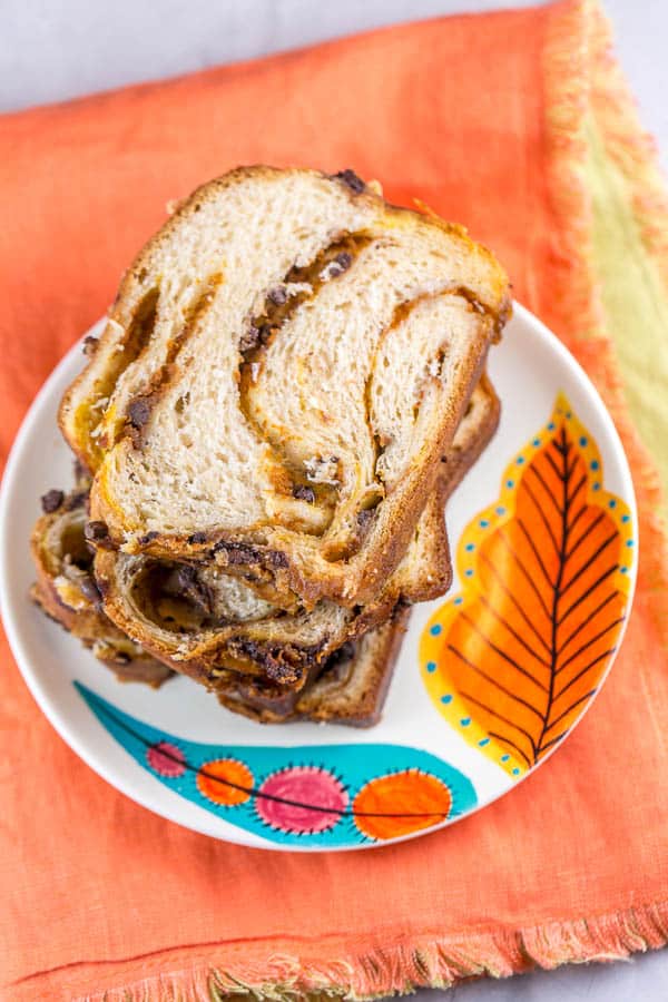 several slices of pumpkin chocolate chip babka stacked on a fall themed dessert plate placed on an orange cloth placemat.