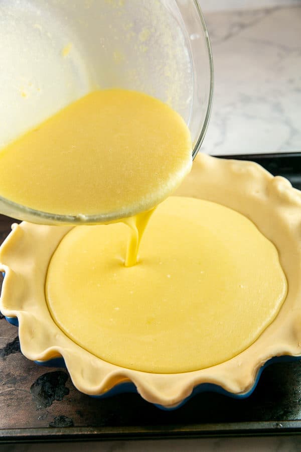pouring buttermilk pie custard into a chilled pie crust on a cookie sheet