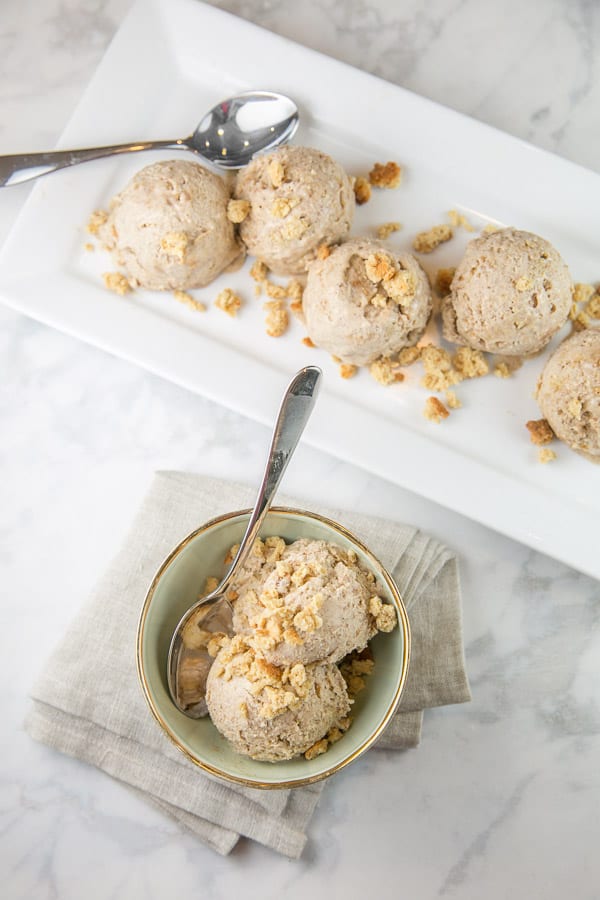two scoops of oatmeal cookie ice cream in a small bowl with more scoops on a rectangular serving dish in the background