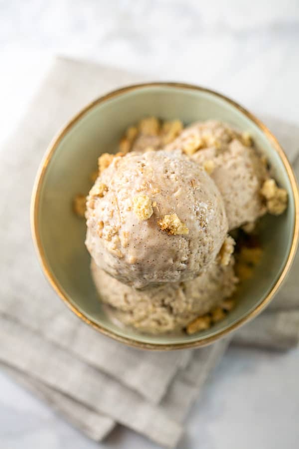 two scoops of oatmeal cookie ice cream in a small dessert bowl with a sprinkle of oatmeal cookie crumbs on top of the ice cream