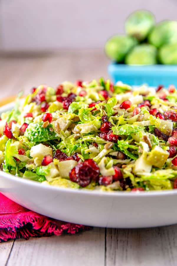 side view of a shaved brussels sprout salad piled high in a white serving bowl with whole brusslels sprouts in the background.