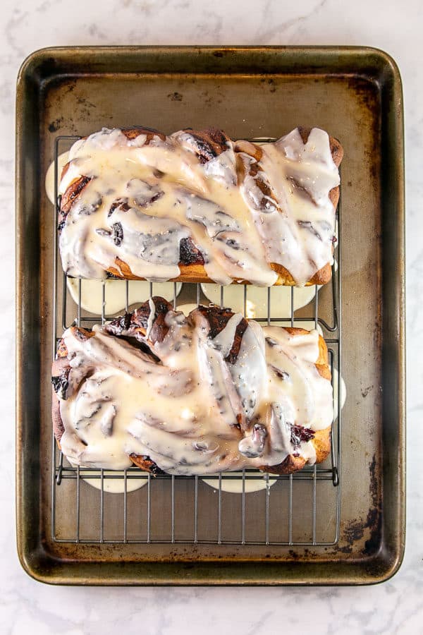 two loaves of cranberry orange babka on a cooling sheet covered in an orange glaze dripping down the babka and pooling on a cookie sheet