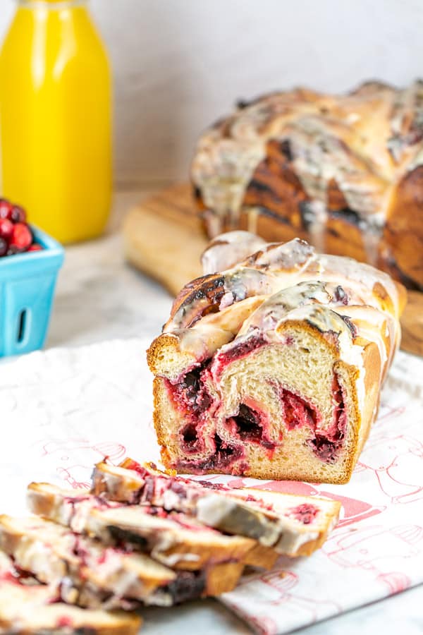 a loaf of cranberry orange babka with several slices removed to show the red swirls of cranberries inside.