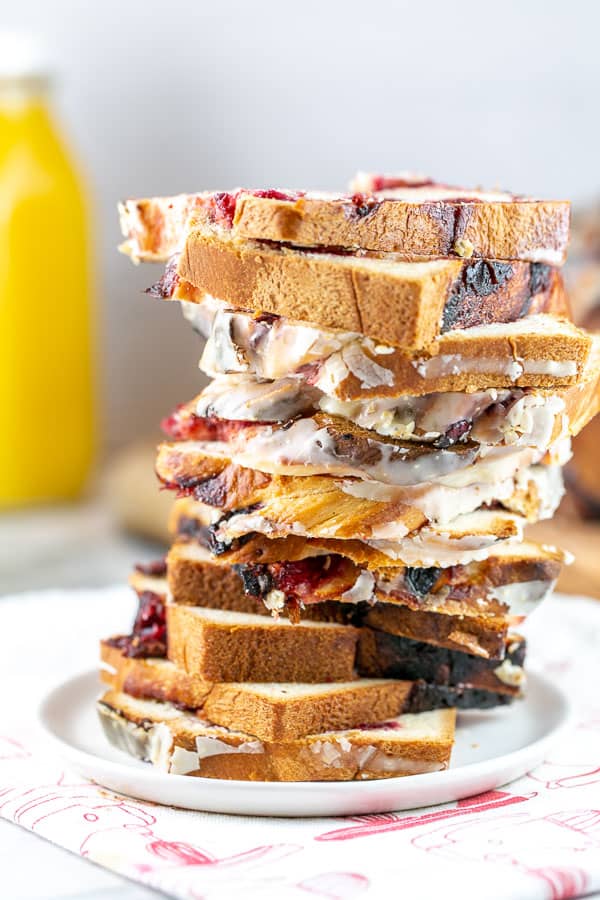 a tall stack of slices of cranberry orange babka on a small dessert plate with a jug of orange juice in the background.