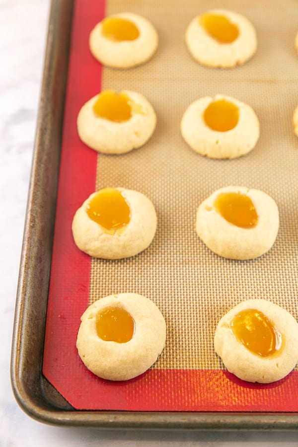 just baked lemon thumbprint cookies filled with lemon curd on a cookie sheet just golden brown with the lemon curd melted and smooth