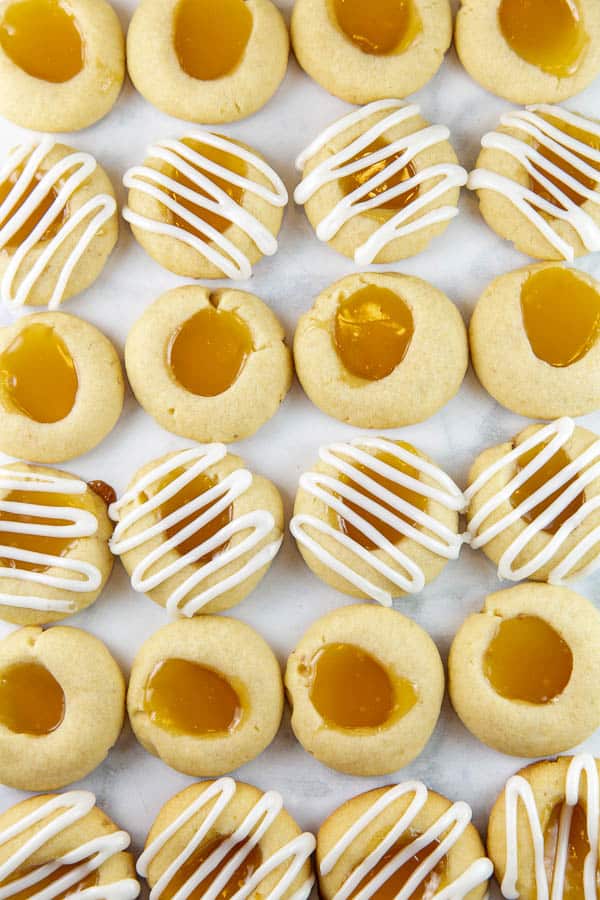 lemon thumbprint cookies filled with lemon curd in rows alternating between plain and covered with squiggles of lemon glaze