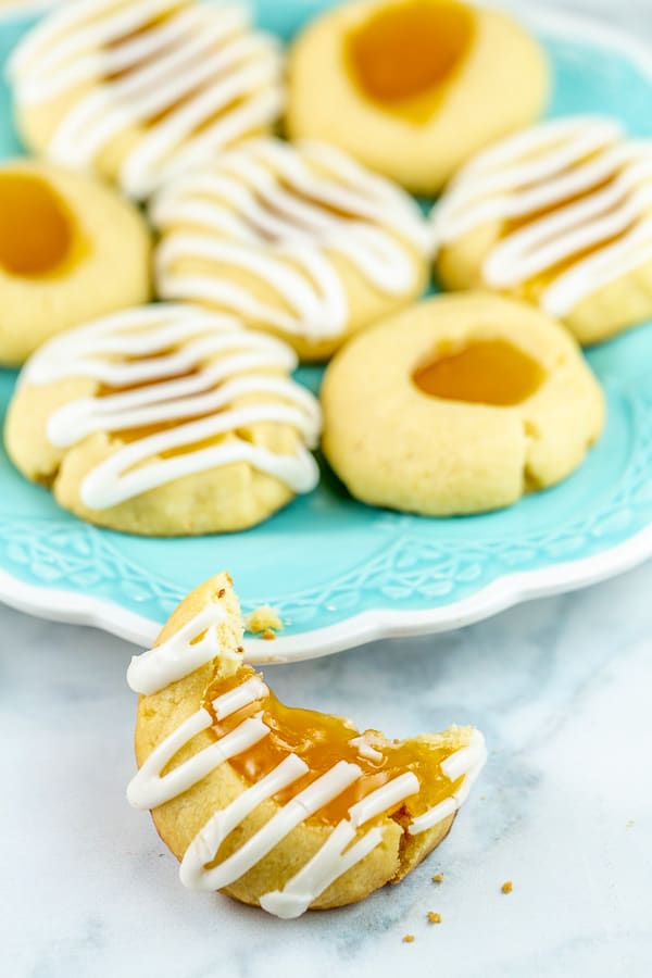 a lemon thumbprint cookie with a large bite taken out of it leaning against a blue dessert plate with a pile of cookies on the plate