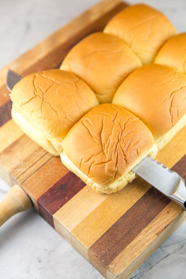 kings hawaiian rolls being sliced open with a serrated knife.
