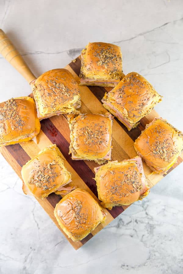 overhead view of baked ham and cheese sliders arranged on a square wooden cutting board.