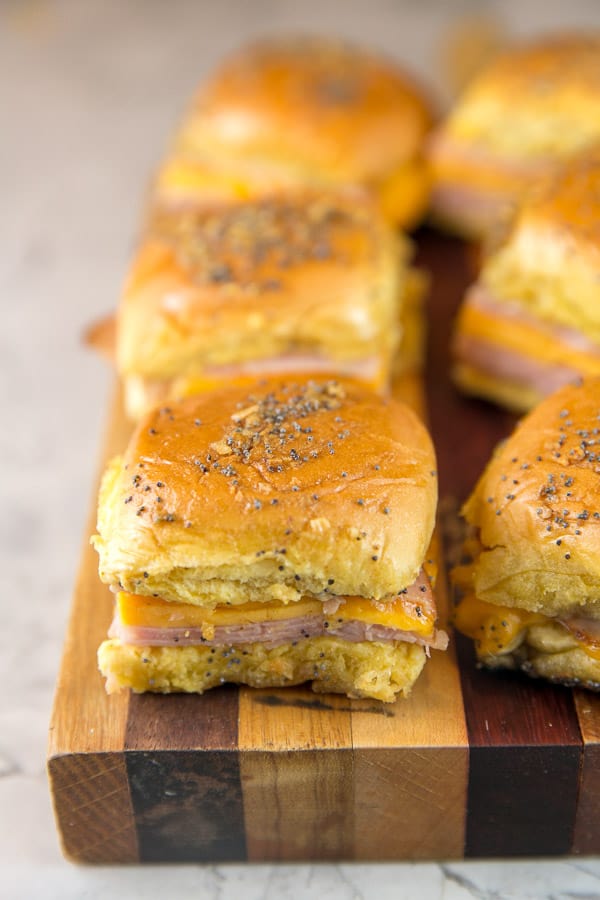 rows of baked ham and cheese sliders on a wooden cutting board.