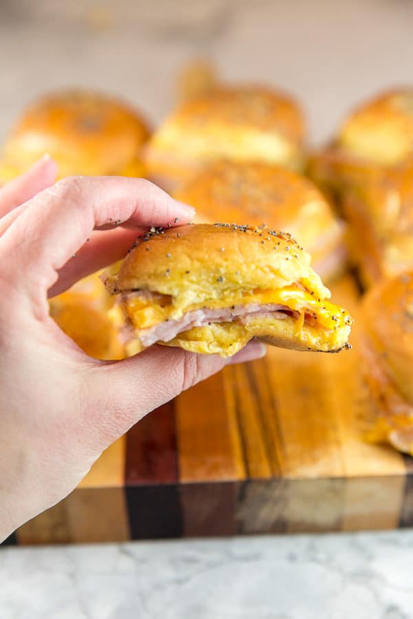 a hand holding a baked ham and cheese slider showing the melted cheese and layer of thinly sliced deli ham