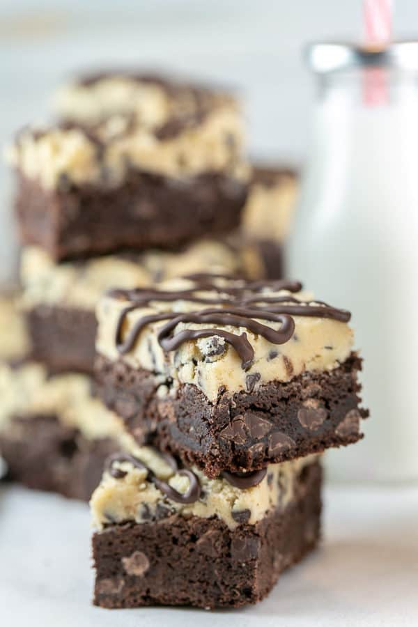 close up of a thick fudgy brownie with a layer of chocolate chip cookie dough on top covered with drizzles of melted chocolate