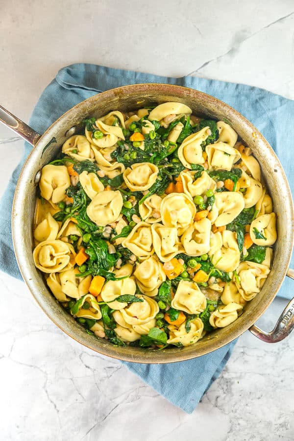 a saute pan filled with tortellini, sweet potatoes, spinach, and white beans