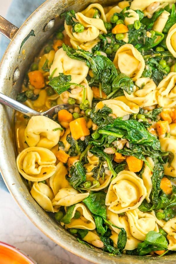 a saute pan filled with tortellini, sweet potatoes, and bright green spinach