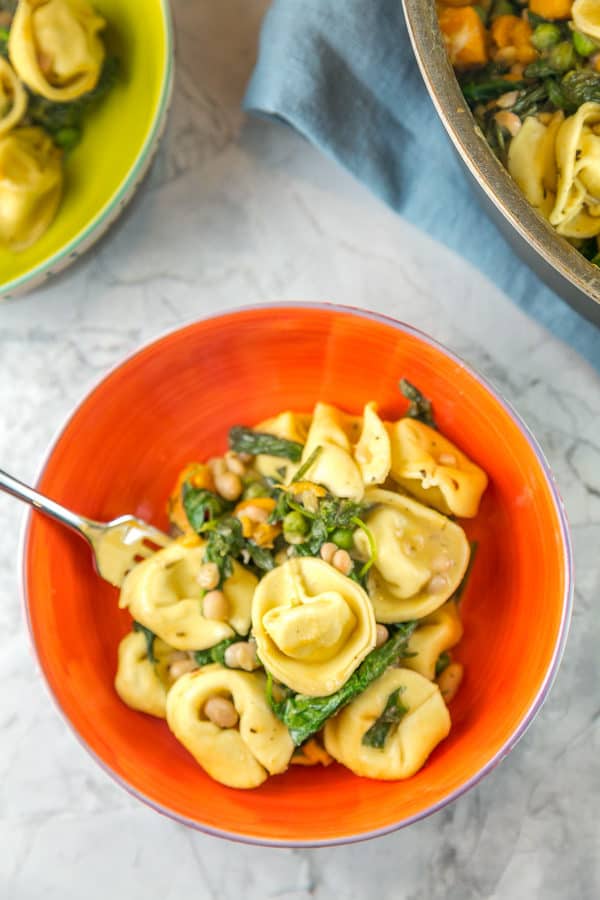a pasta bowl filled with tortellini, sweet potatoes, spinach, white beans, and peas