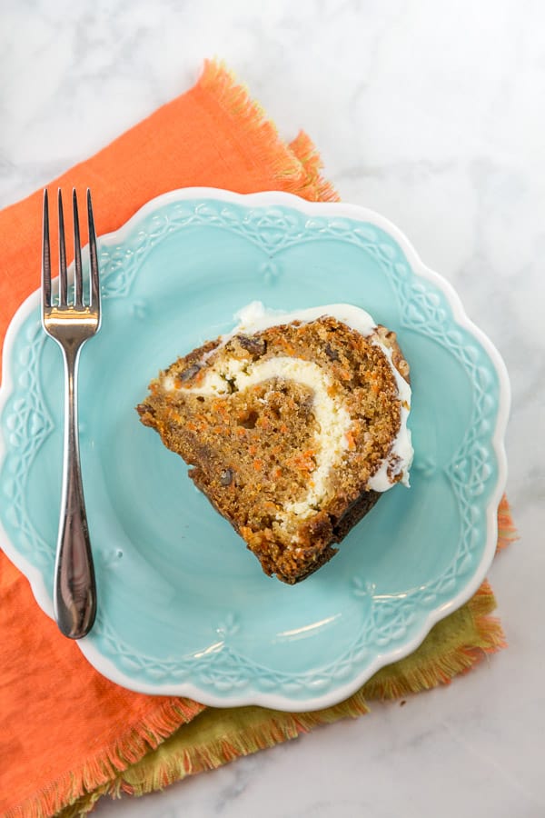 a slice of carrot bundt cake on a blue dessert plate showing a layer of cream cheese frosting baked into the cake.