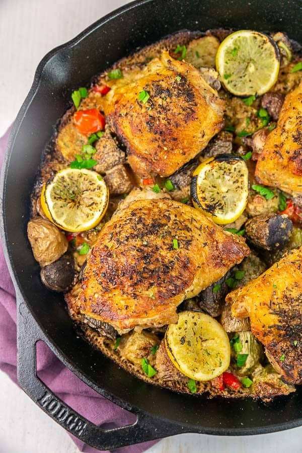 a cast iron skillet filled with chicken, brussels sprouts, and potatoes with a creamy tahini sauce