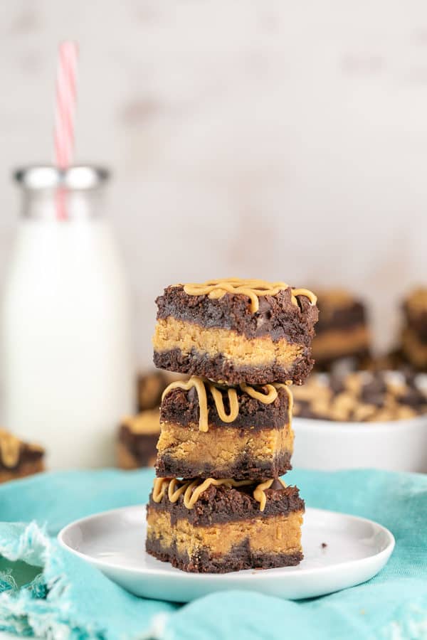 a stack of three thick fudgy brownies filled with peanut butter with more brownies and a milk jug in the background