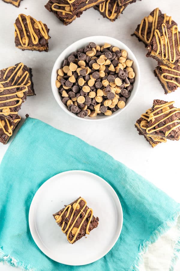 peanut butter brownies with a peanut butter drizzle surrounding a bowl of chocolate and peanut butter chips