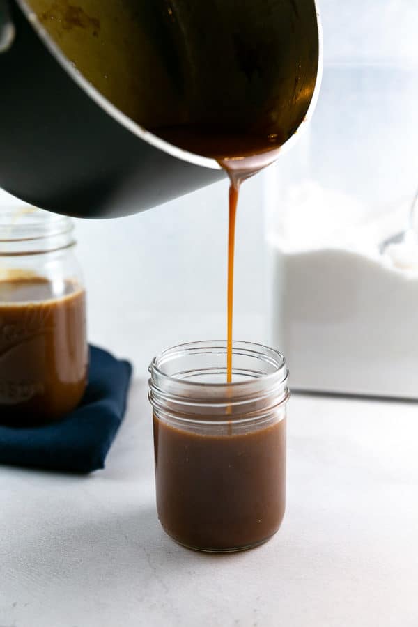 pouring caramel sauce from a saucepan into a glass jar