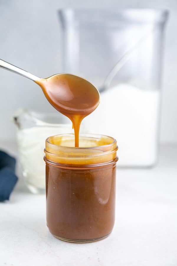 caramel sauce dripping from a spoon into a jar