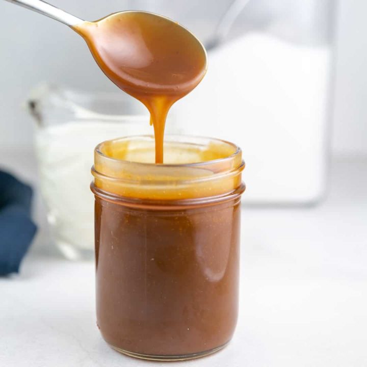 a spoon drizzling caramel sauce into a jar