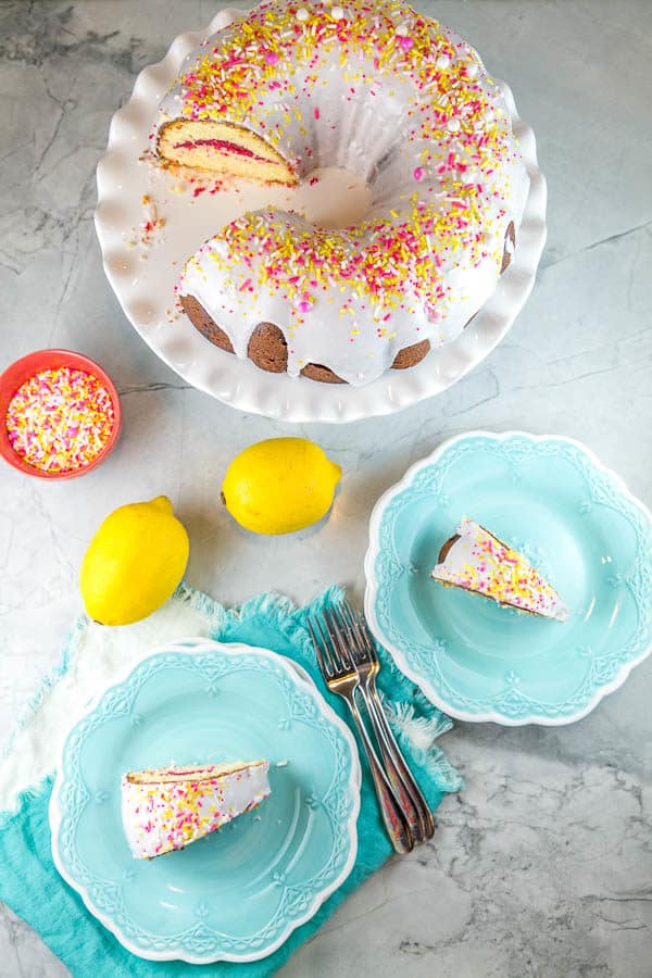 two slices of pink lemonade bundt cake on blue dessert plates with lemons and sprinkles