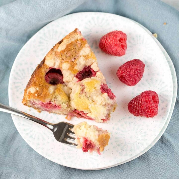 slice of raspberry crumb cake on a dessert plate with fresh raspberries on the side