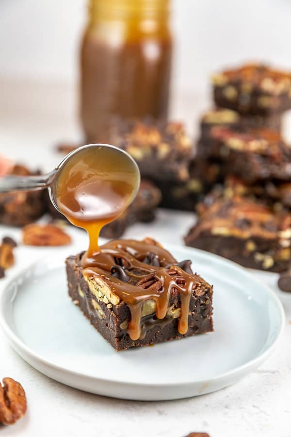a spoon drizzling caramel sauce on a fudgy brownie