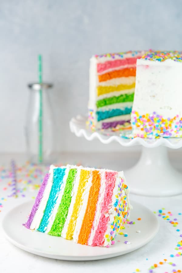 slice of rainbow cake in front of the rest of the colorful cake