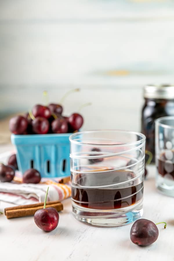glass with cherry bounce and fresh cherries visible in the background