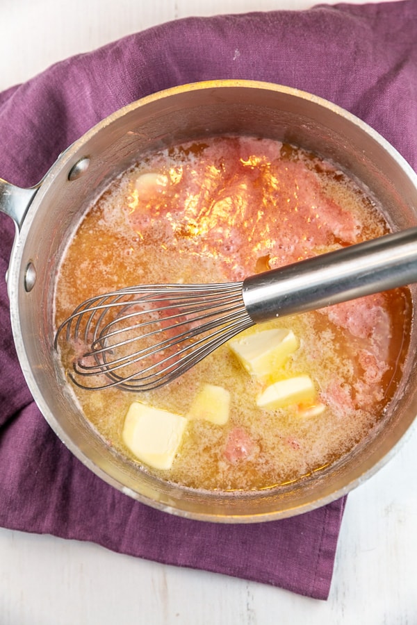 vanilla cherry fudge frosting in a saucepan with melting pats of butter