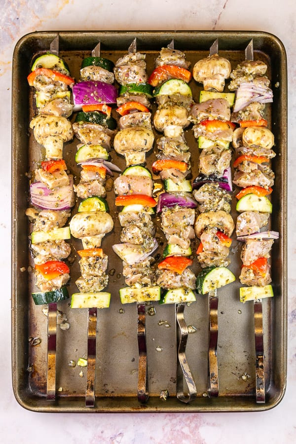 long metal skewers with chicken and vegetables on a cookie sheet