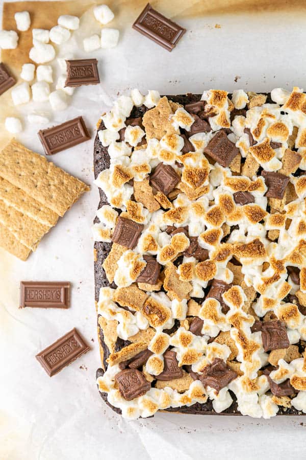 uncut brownies topped with toasted marshmallows, chocolate pieces, and graham crackers