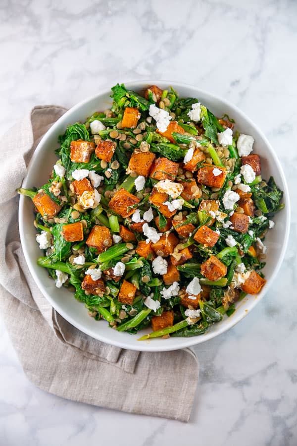 large white bowl filled with butternut squash, turnip greens, and lentil salad.