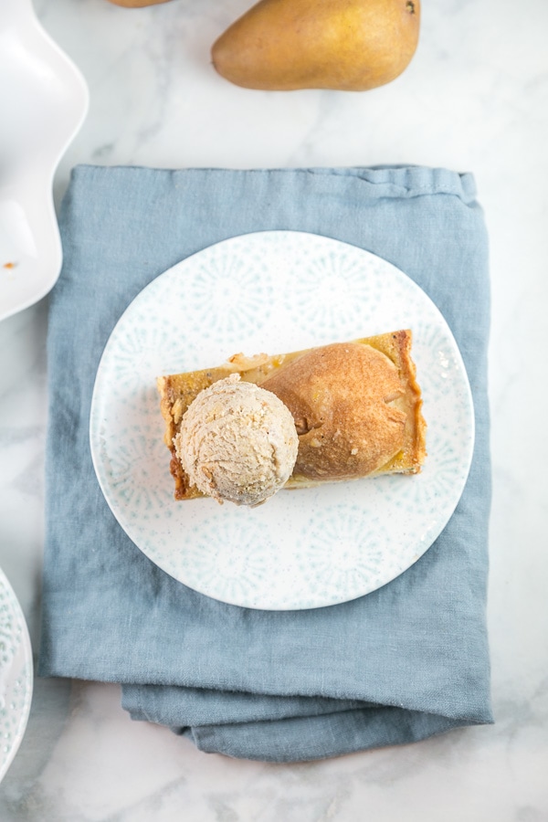 slice of brown butter pear tart with a scoop of oatmeal cookie ice cream on a blue and white dessert plate.