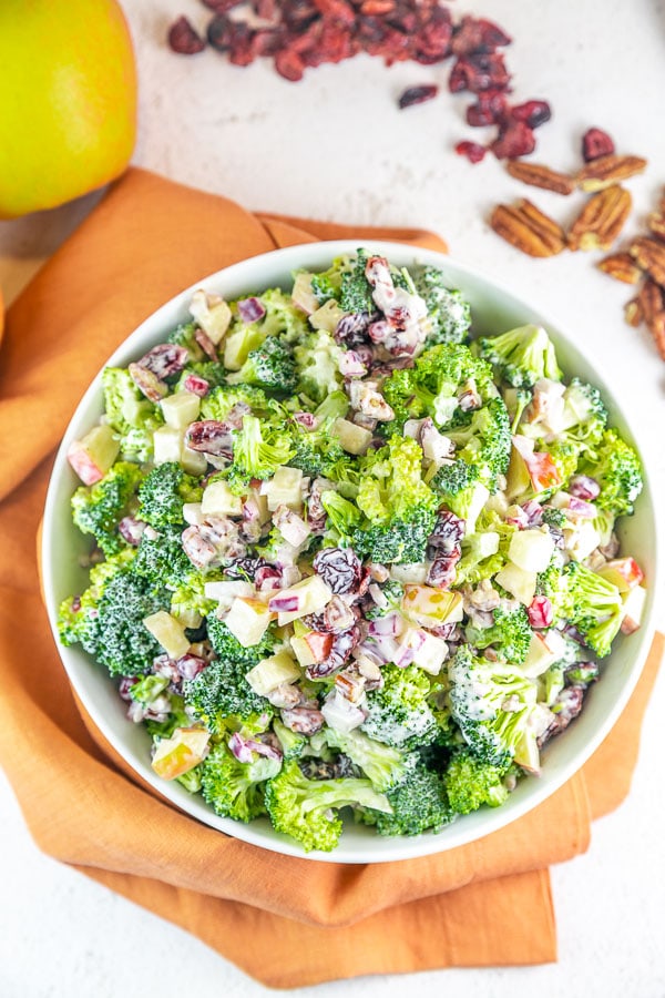 broccoli salad with apples and craisins in a large white bowl