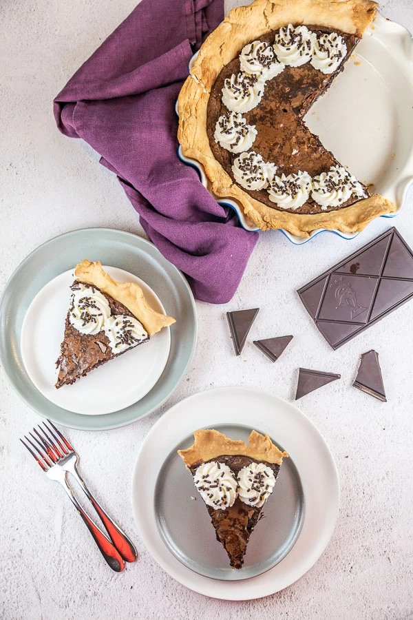 two pieces of pie on dessert plates with chopped chocolate in the background
