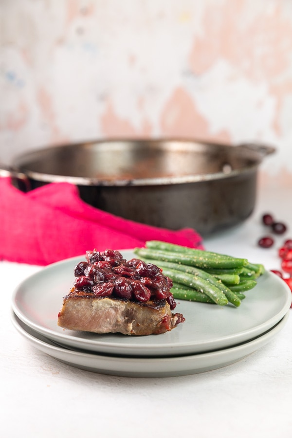 pork chop and green beans on a dinner plate with a saute pan in the background