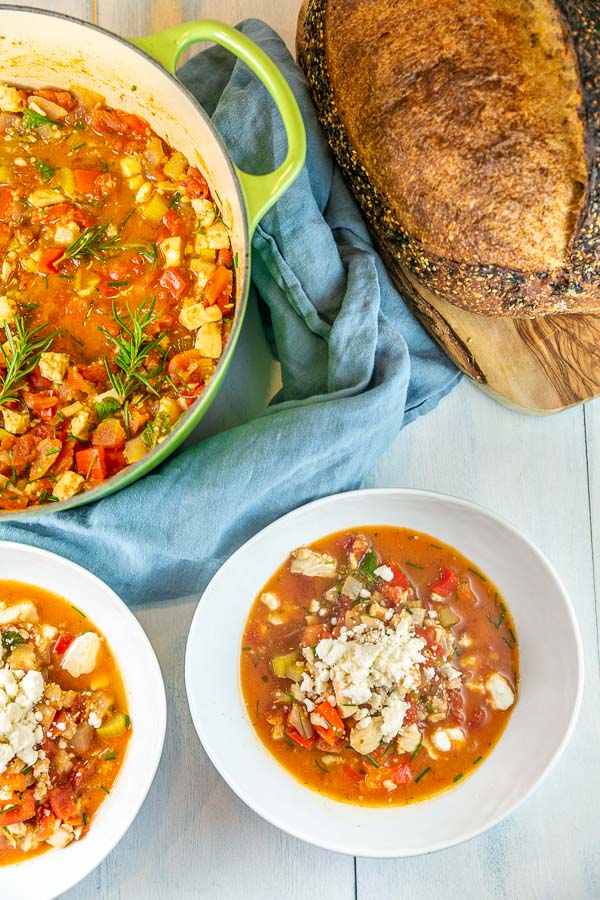 two bowls of soup with a dutch oven and loaf of bread in the background