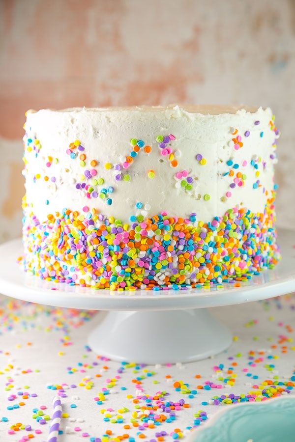 three layer funfetti cake covered with white frosting and pastel candy quins