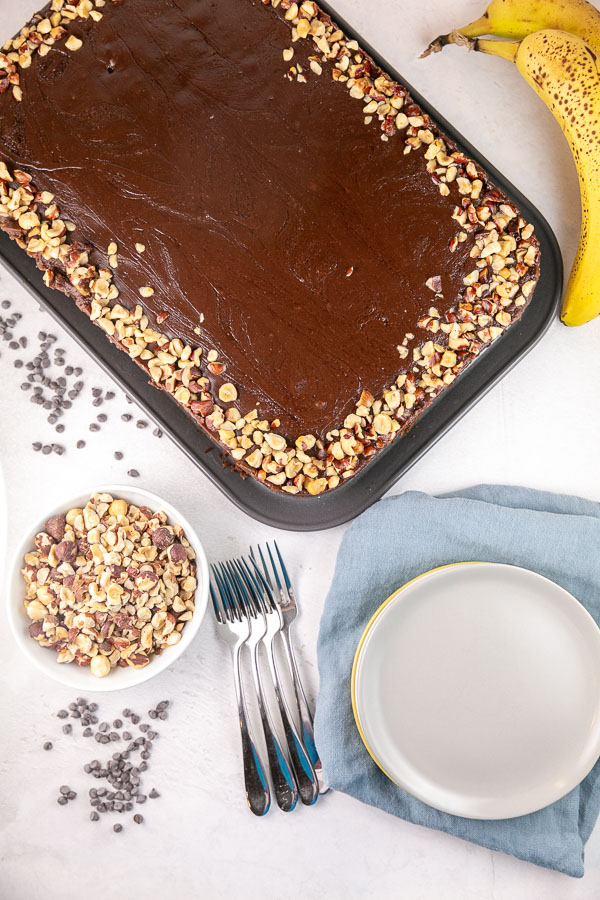 banana nutella snack cake in the pan covered with nutella glaze and chopped hazelnuts