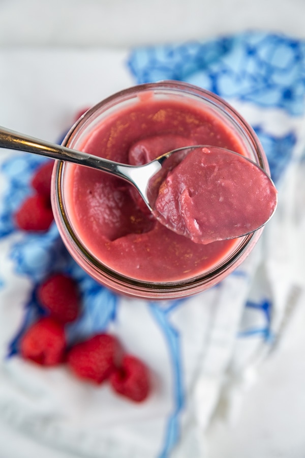 bright pink raspberry curd in a mason jar with a spoonful resting on top