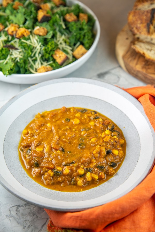 bowl of pumpkin soup with sausage and black beans with a salad and loaf of bread.